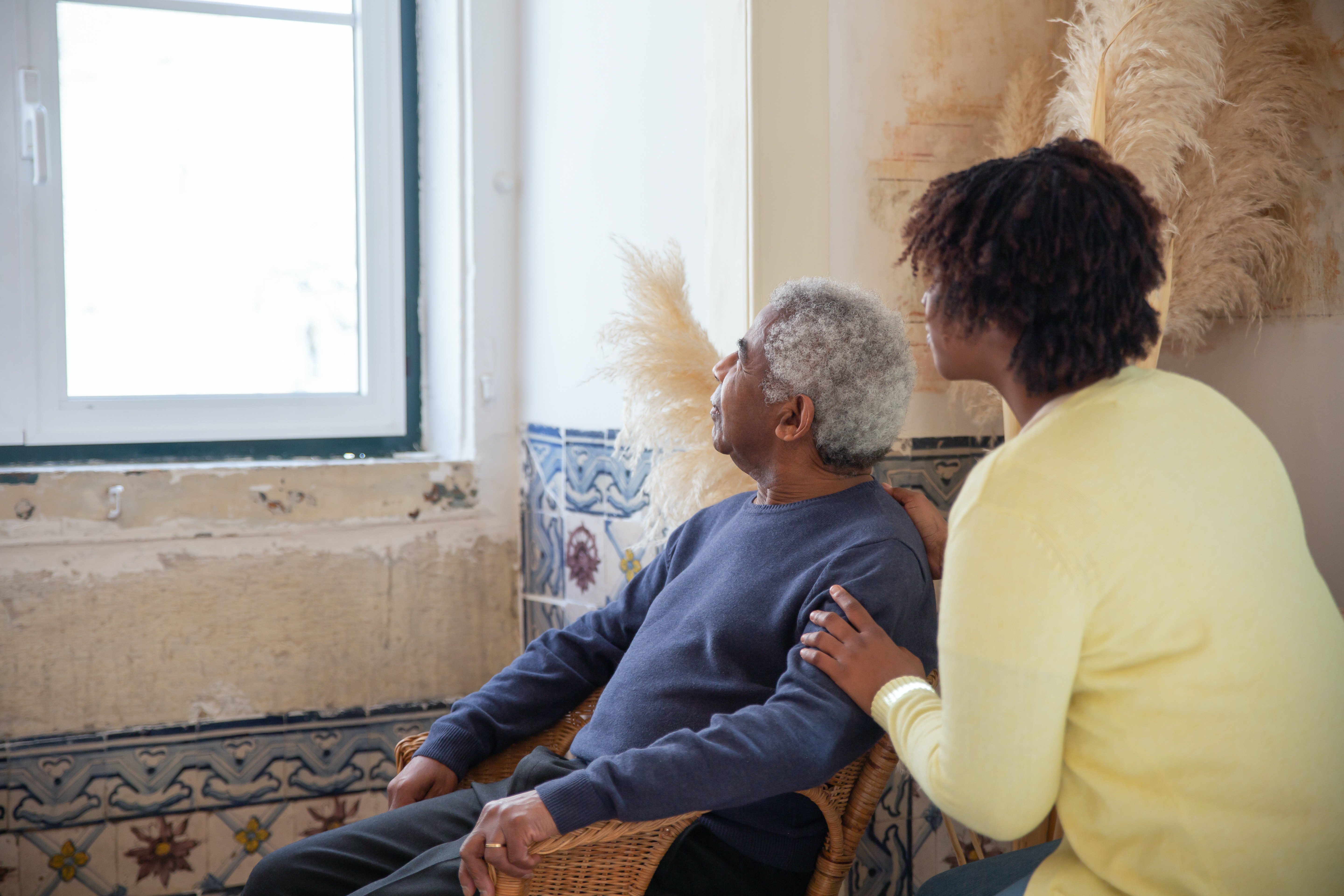 woman giving an elderly man care while he is staring at the window